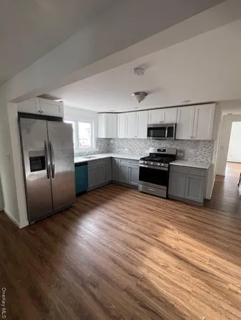 a kitchen with stainless steel appliances granite countertop a refrigerator a stove oven a sink dishwasher and white cabinets with wooden floor