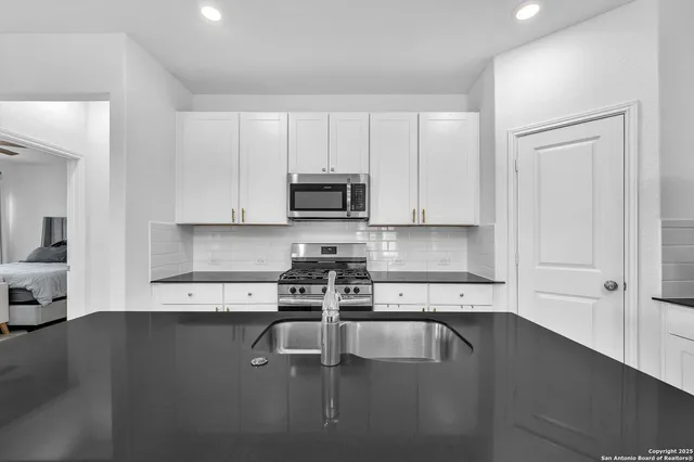 a kitchen with granite countertop a stove a sink and a white cabinets