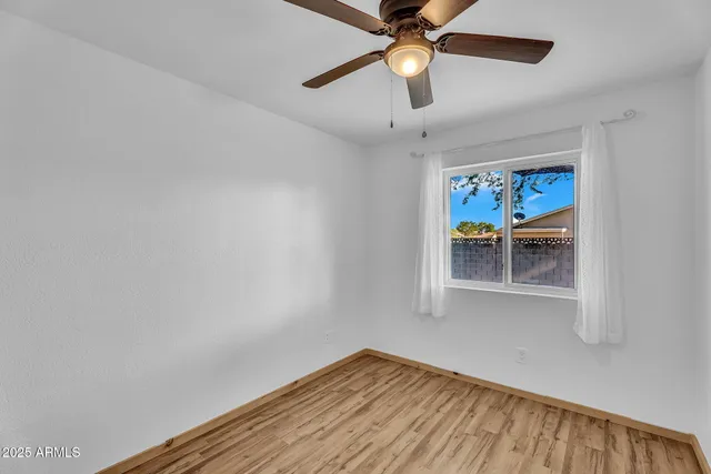 a view of an empty room with wooden floor and a ceiling fan