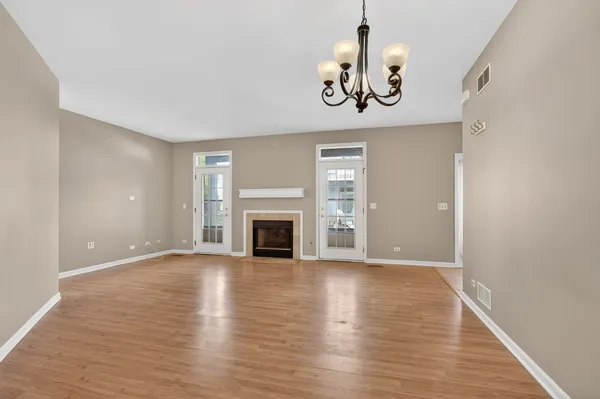 an empty room with wooden floor chandelier and windows