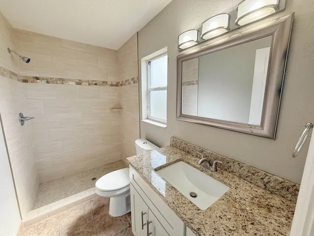 a bathroom with a granite countertop sink toilet a mirror and shower