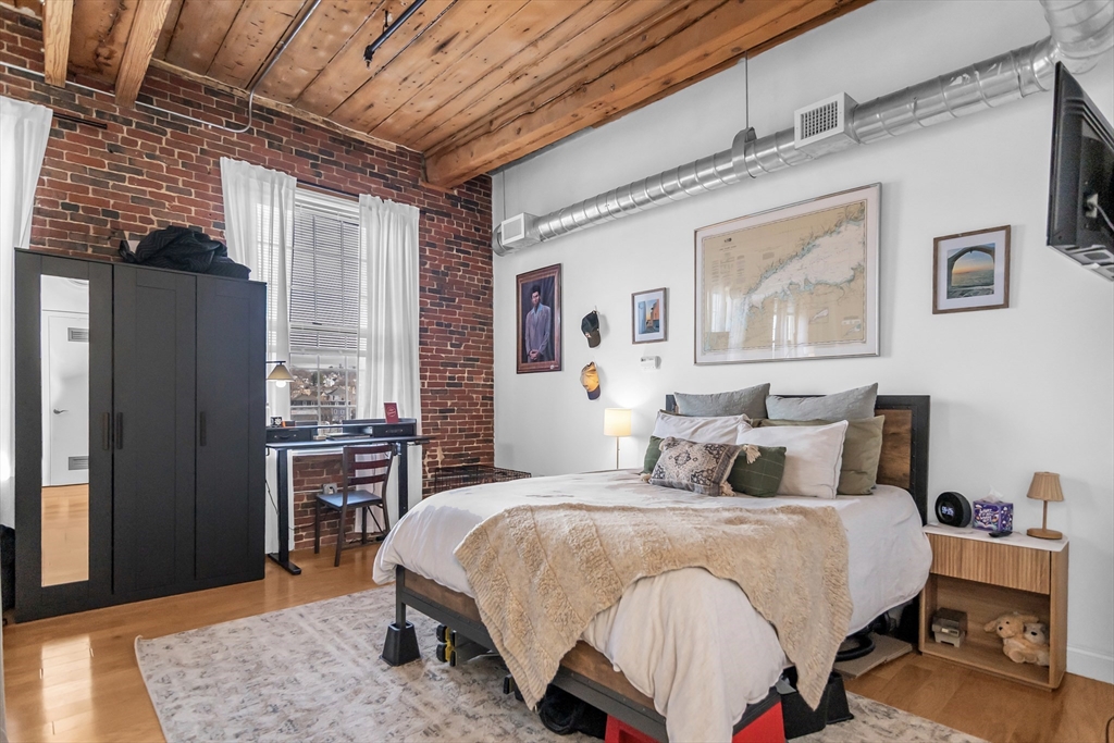 130 John Street, Unit 216 Lowell, MA 01852 - Photo 6 of 17 a bedroom with a bed a table and painting on the wall
