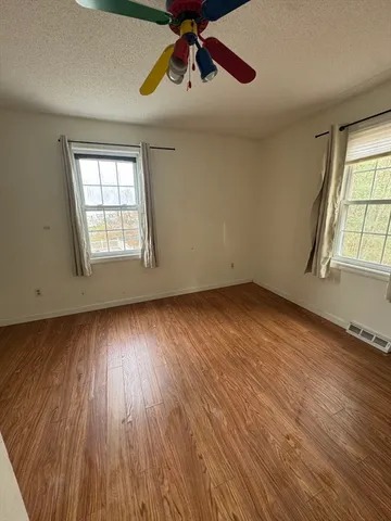 an empty room with wooden floor chandelier fan and windows