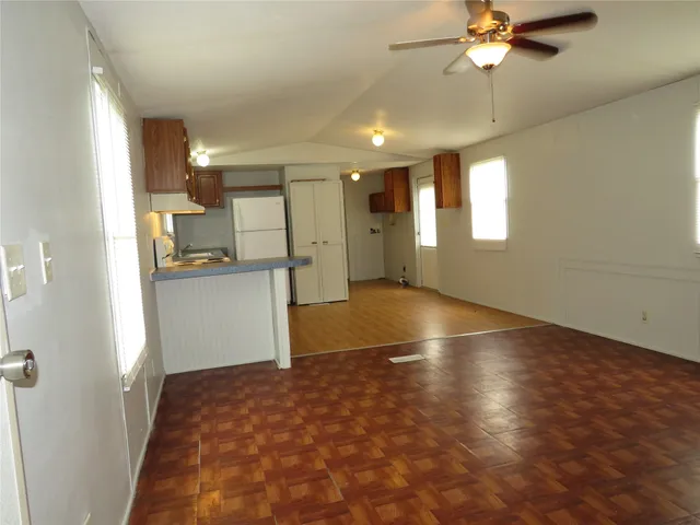 an empty room with wooden floor and kitchen view