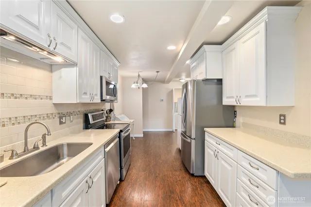 a kitchen with stainless steel appliances a sink dishwasher a refrigerator and wooden cabinets with wooden floor
