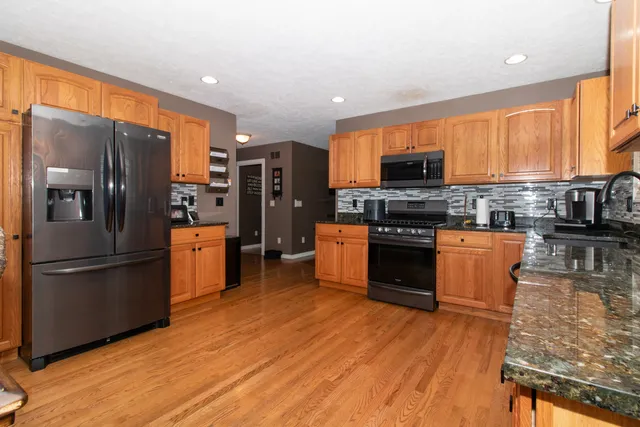 a kitchen with stainless steel appliances granite countertop a refrigerator a stove a dining table and chairs with wooden floor