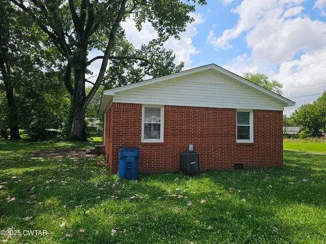 a backyard of a house with plants and large tree
