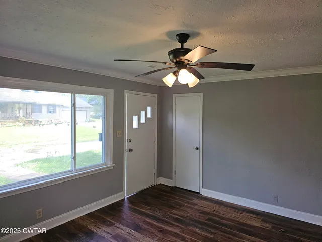 an empty room with wooden floor fan and windows