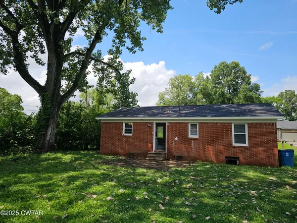 a backyard of a house with plants and large tree