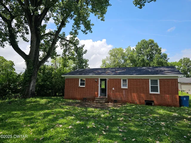 a backyard of a house with plants and large tree
