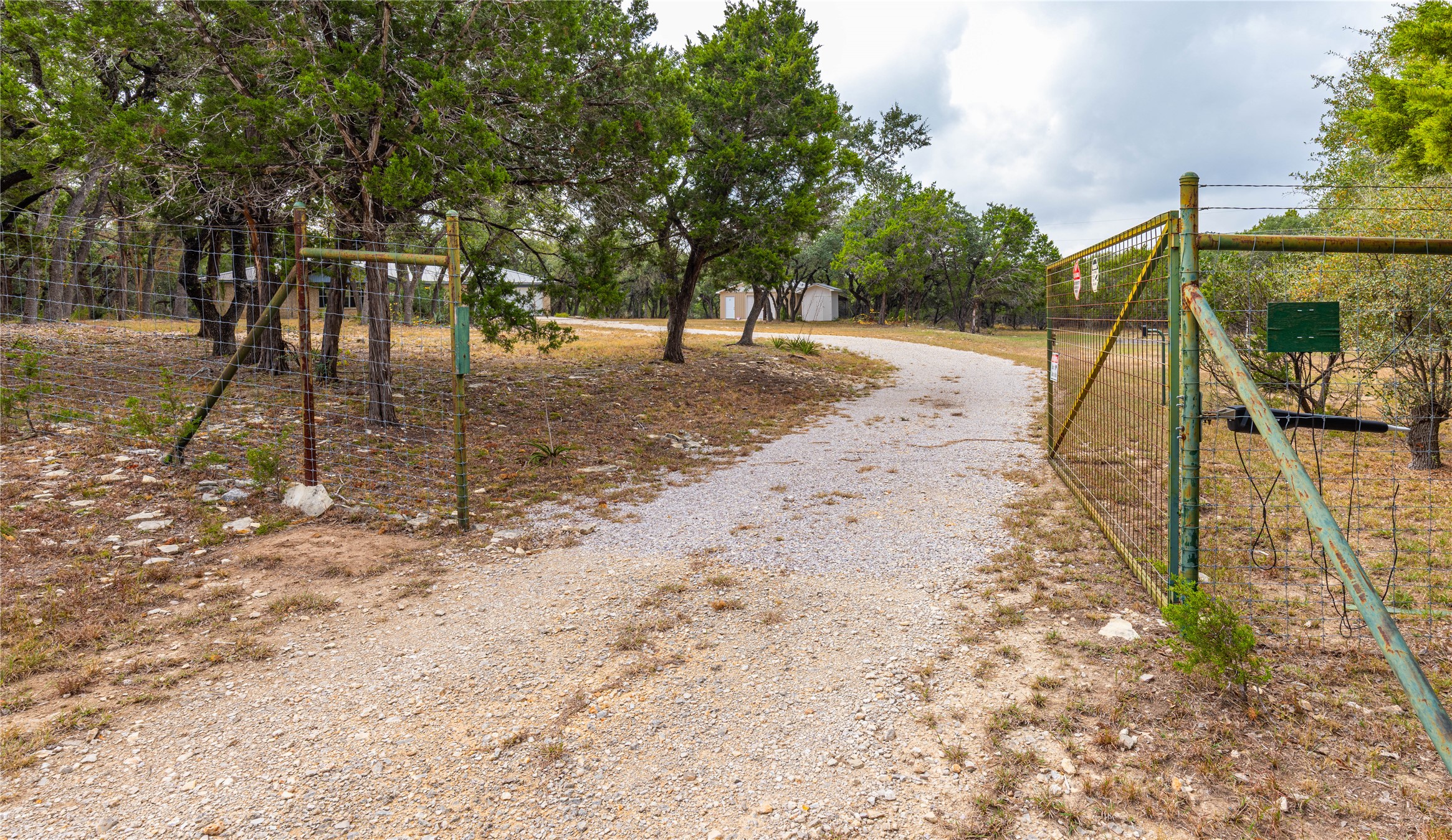 2501 Fischer Store Road Wimberley, TX 78676 - Photo 21 of 23 Gated gravel driveway extending through a wooded landscape