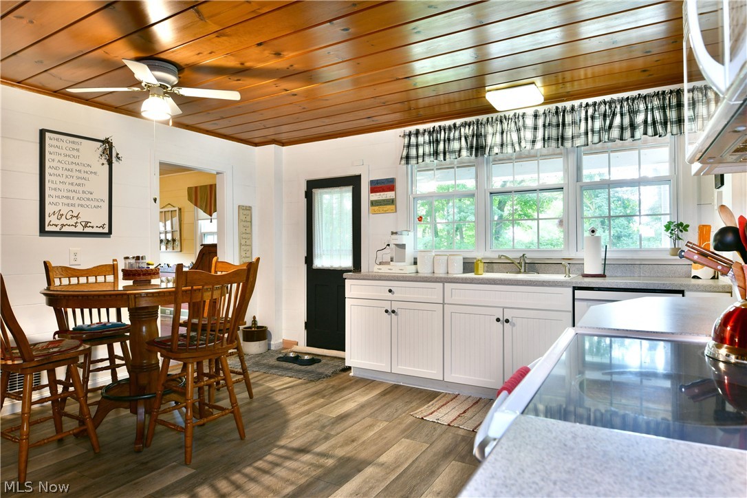 8683 King Graves Road Northeast Warren, OH 44484 - Photo 6 of 50 Kitchen space featuring wood-finish flooring, a wood-paneled ceiling with a ceiling fan, white cabinetry with black hardware, and a three-pane window above the sink