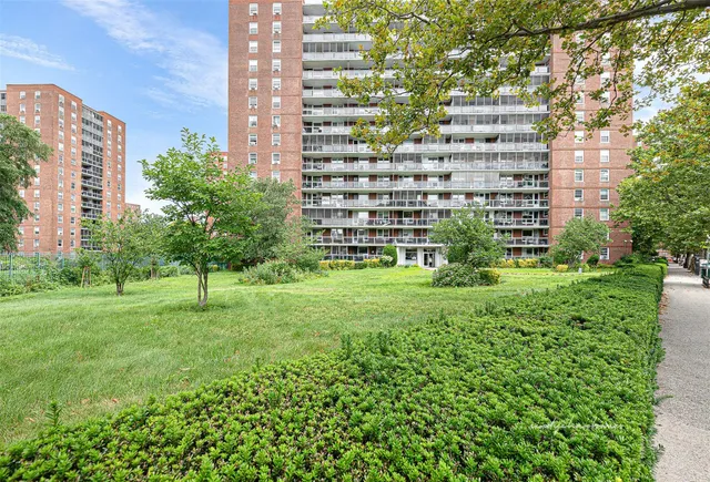 a view of a tall building next to a big yard and large trees