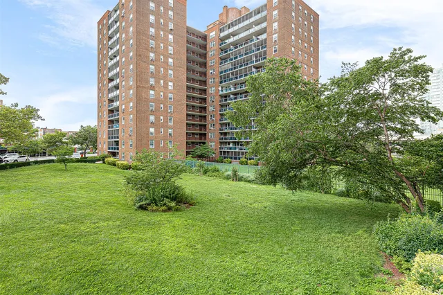 a view of a tall building next to a big yard and large trees