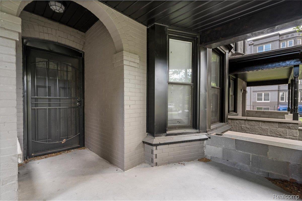 58 East Philadelphia Street Detroit, MI 48202 - Photo 4 of 24 Covered front porch featuring a security screen door, an arched brick entryway, a black painted ceiling, and a concrete floor