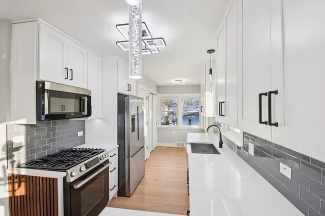 a kitchen with stainless steel appliances granite countertop a refrigerator a stove oven a sink dishwasher and white cabinets with wooden floor