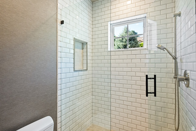 3 Carriagewood Cove, Unit 1088 Sandy, UT 84092 - Photo 41 of 79 Shower enclosure featuring subway tile surround, clear glass paneling, built-in shower niche, brushed nickel showerhead and fixtures, and a high-set window