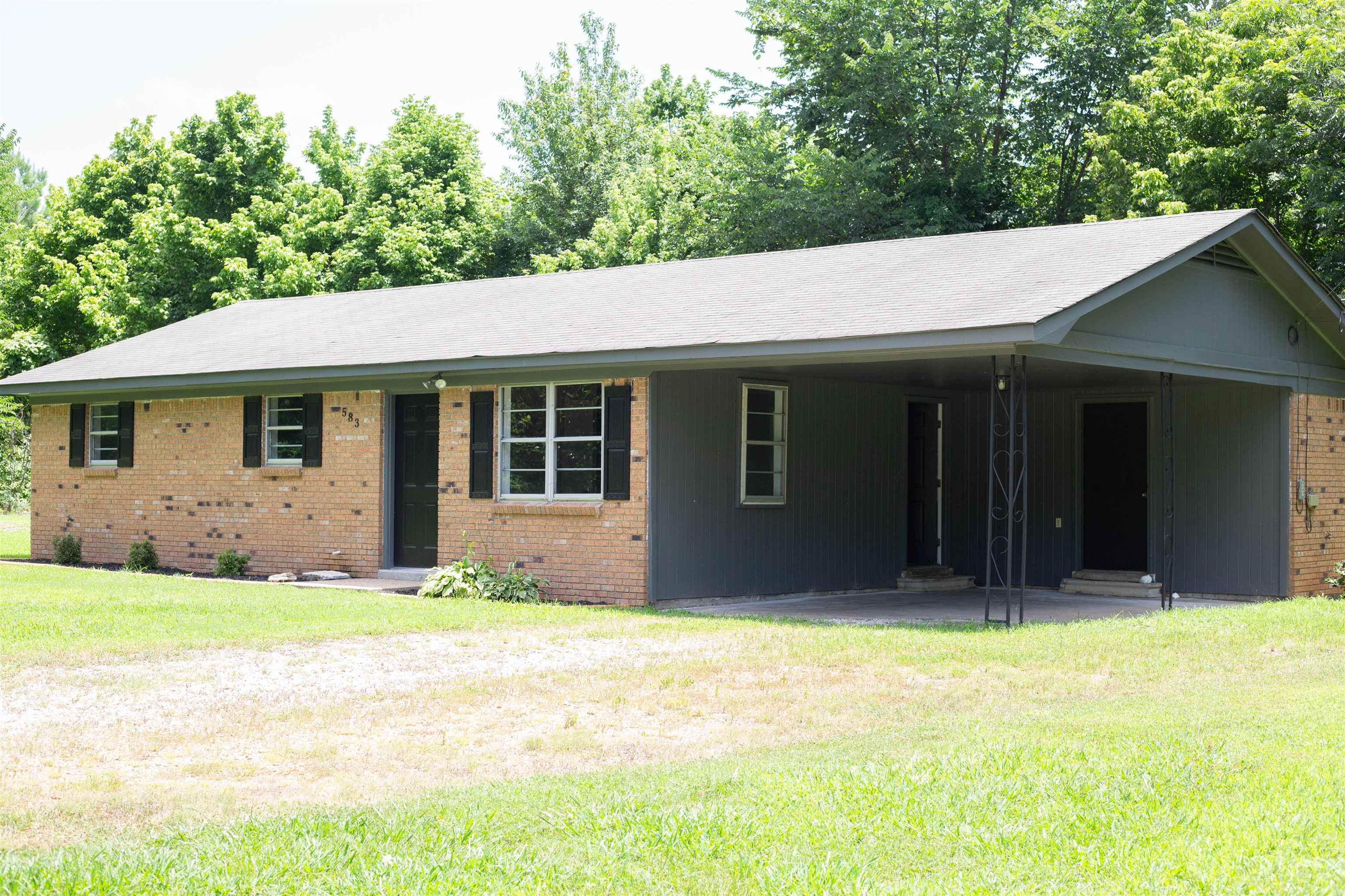 583 Armstrong Road Drummonds, TN 38023 - Photo 3 of 14 Brick and siding exterior featuring a carport with decorative metal posts, multiple windows with dark shutters, and a gravel driveway