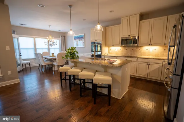 a kitchen with stainless steel appliances granite countertop a stove a refrigerator a kitchen island a dining table and chairs with wooden floor