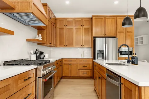 a kitchen with stainless steel appliances a sink a stove and a dining table with wooden floor