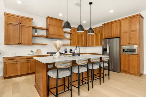 a kitchen with stainless steel appliances granite countertop a refrigerator a sink dishwasher a dining table and chairs with wooden floor