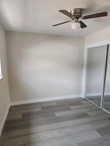 an empty room with wooden floor chandelier fan and windows