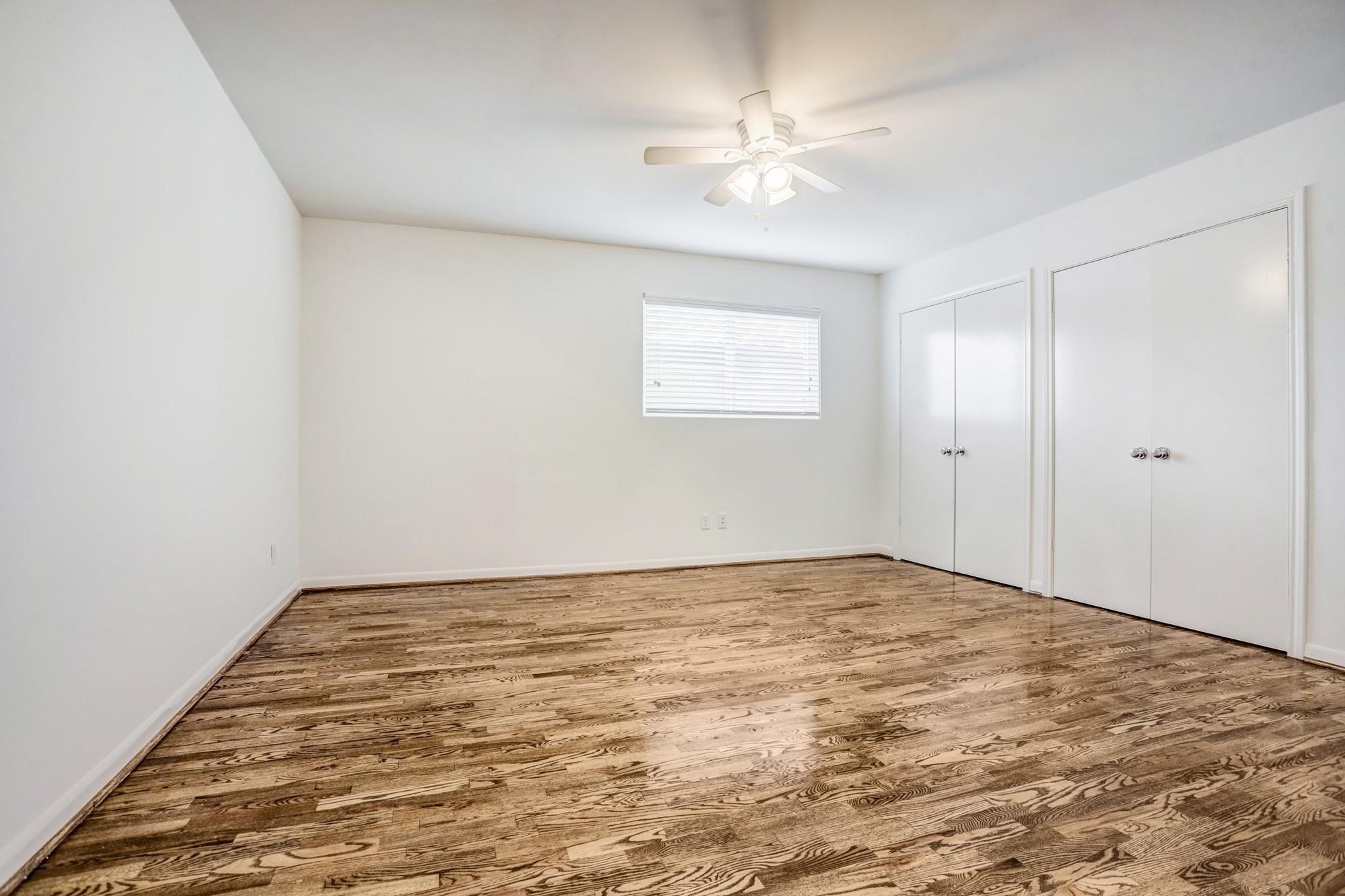 415 Hawthorne Street, Unit 4 Houston, TX 77006 - Photo 6 of 7 This room features polished hardwood floors, a ceiling fan, and ample natural light from a window. It includes two spacious closets with white doors, offering plenty of storage space.