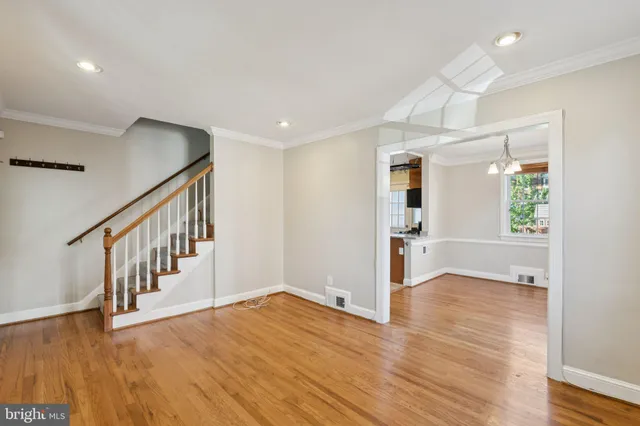 a view of an empty room with wooden floor and a kitchen