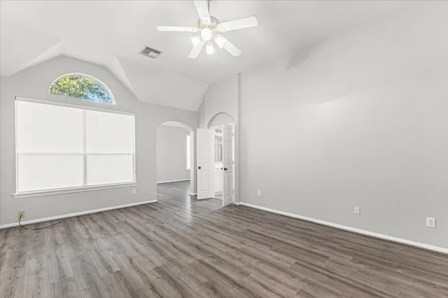an empty room with wooden floor ceiling fan and windows