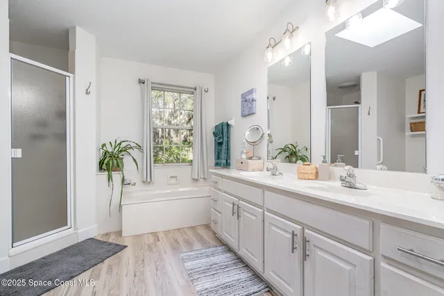 a spacious bathroom with a double vanity sink a large mirror a bathtub and next to a window