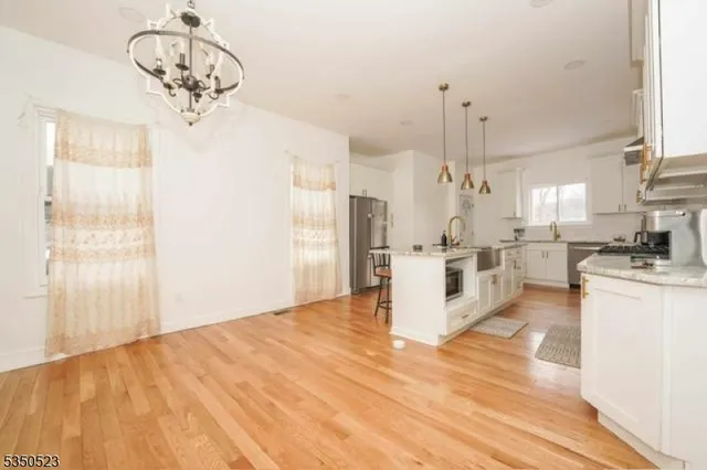 a kitchen with stainless steel appliances kitchen island granite countertop a refrigerator a stove and white cabinets with wooden floor