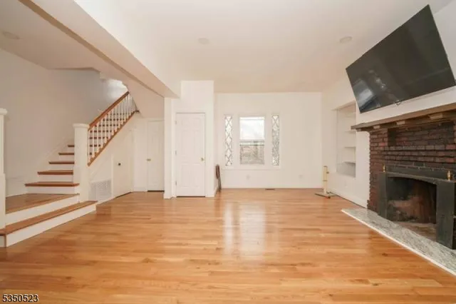 a view of an empty room with wooden floor fireplace and a window