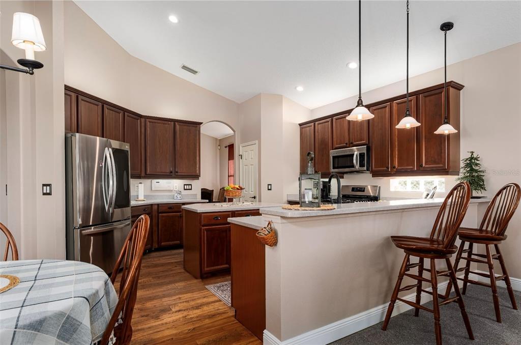 6552 Tailfeather Way Bradenton, FL 34203 - Photo 11 of 65 a kitchen with stainless steel appliances granite countertop a refrigerator a stove top oven a sink dishwasher a dining table and chairs with wooden floor