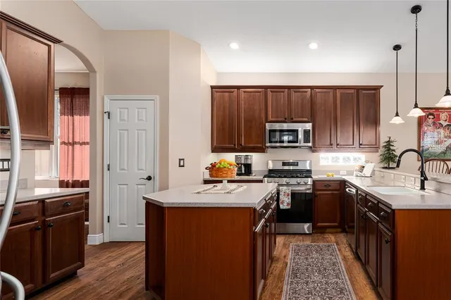 a kitchen with stainless steel appliances granite countertop a refrigerator a stove top oven a sink dishwasher a dining table and chairs with wooden floor
