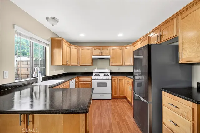 a kitchen with stainless steel appliances granite countertop a refrigerator a sink dishwasher a stove and white countertops with wooden floor