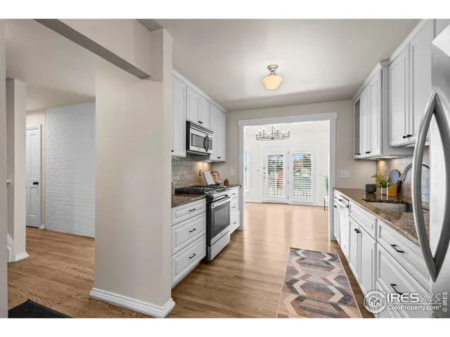 a kitchen with stainless steel appliances granite countertop a stove top oven a sink dishwasher and white cabinets with wooden floor