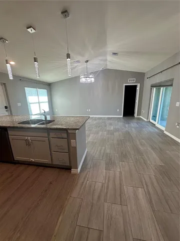a room with kitchen island granite countertop wooden floors and a sink