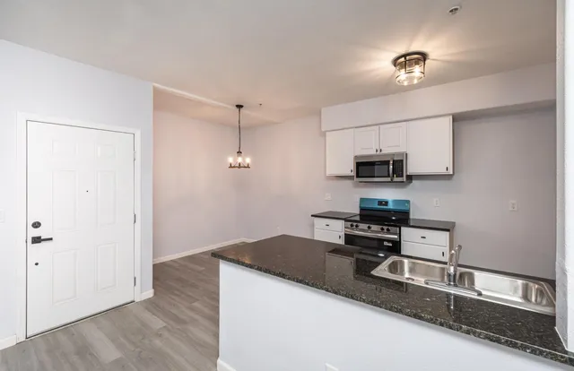 a kitchen with stainless steel appliances granite countertop a sink a stove a refrigerator a microwave oven with white cabinets and wooden floor