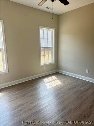 an empty room with wooden floor chandelier fan and windows