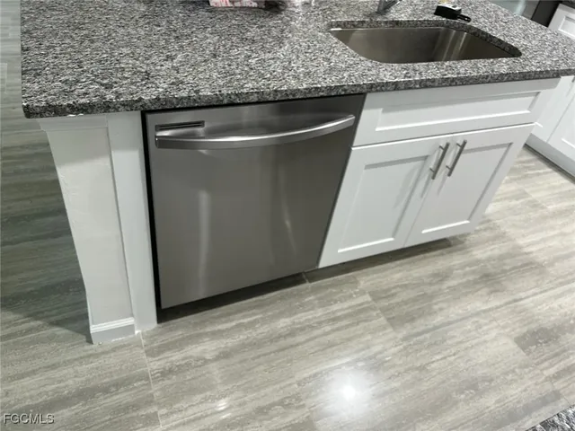 a large kitchen with stainless steel appliances a sink a stove a refrigerator and white cabinets with wooden floor