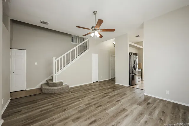a view of an empty room with wooden floor and a ceiling fan