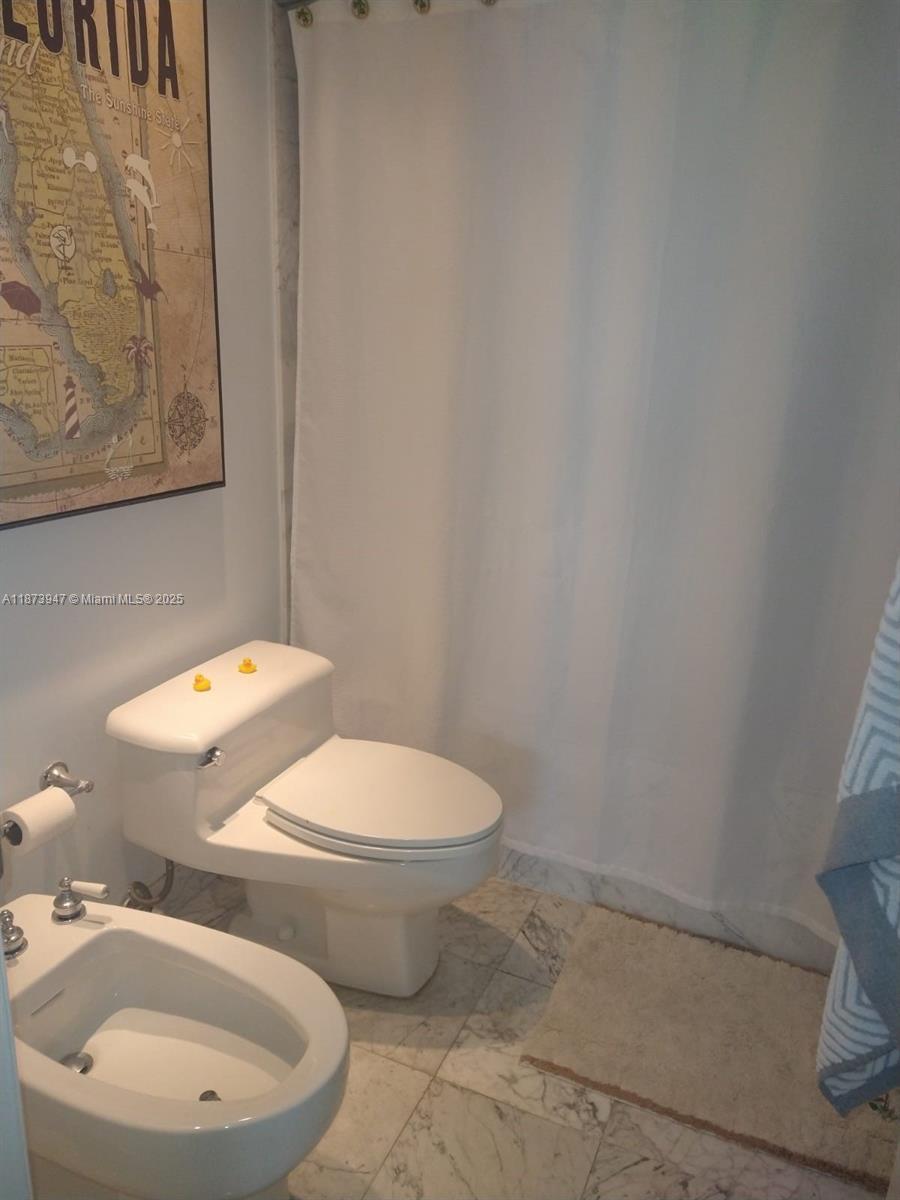 9341 Collins Avenue, Unit 806 Surfside, FL 33154 - Photo 12 of 27 a white toilet sitting next to a white sink and vanity