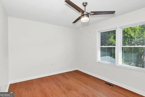 an empty room with wooden floor fan and windows