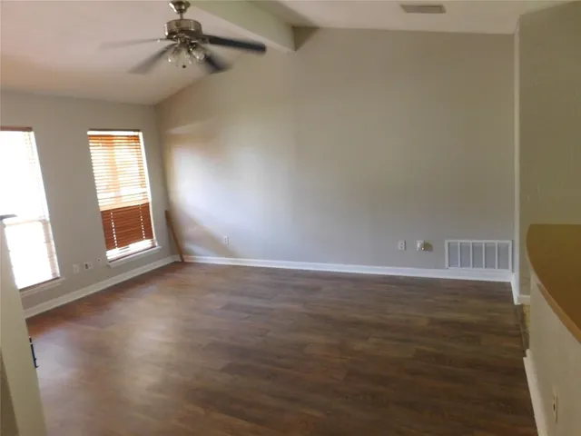 an empty room with wooden floor fan and windows