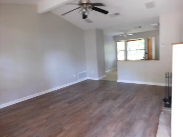 an empty room with wooden floor chandelier fan and windows