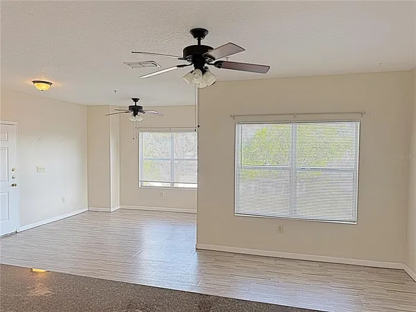 an empty room with wooden floor chandelier fan and windows