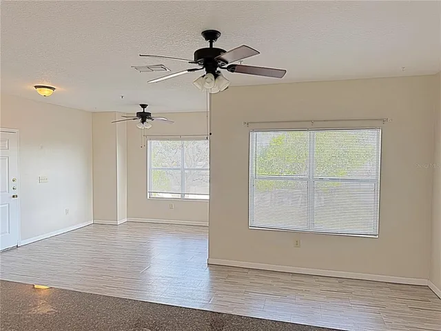 an empty room with wooden floor chandelier fan and windows