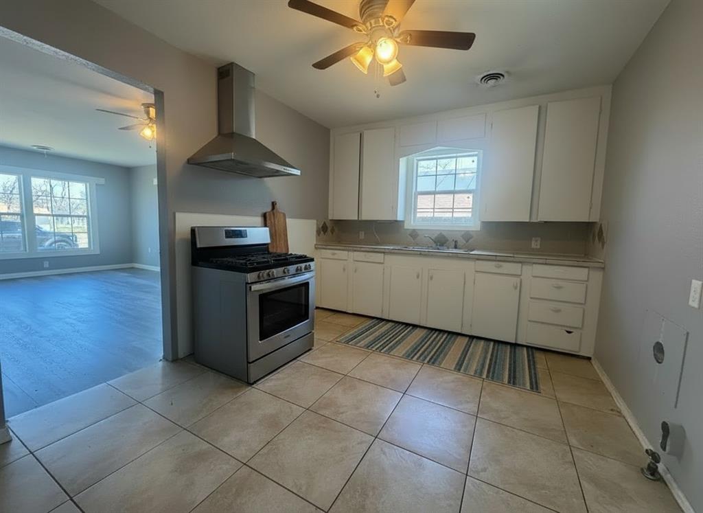 3520 Colcord Avenue Waco, TX 76707 - Photo 5 of 17 Virtually Staged Kitchen featuring a ceiling fan, gas range, light countertops, white cabinetry, and plenty of natural light