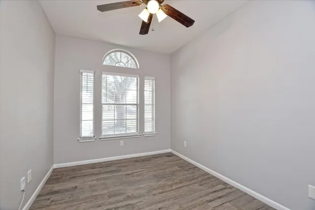 an empty room with wooden floor chandelier fan and windows