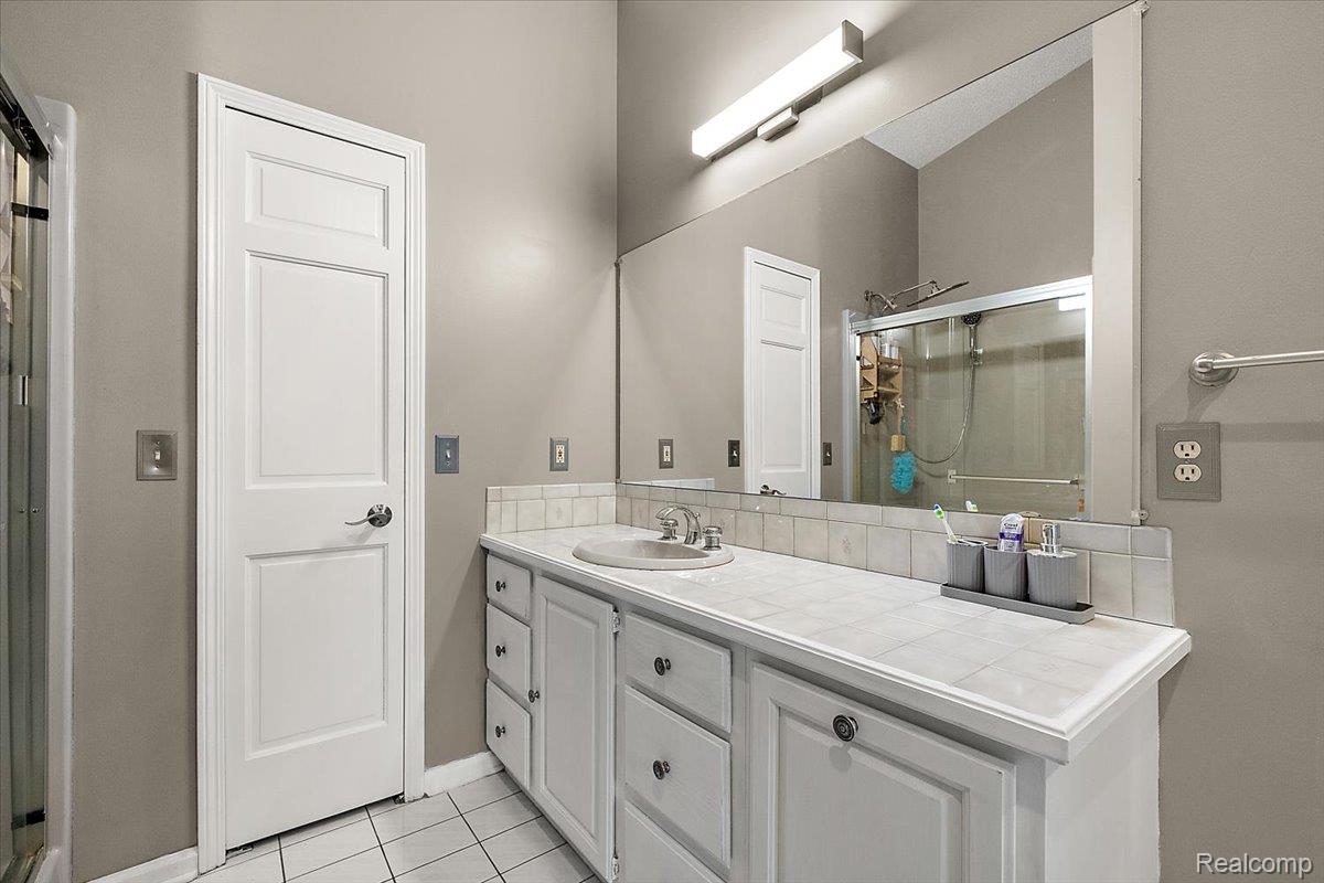 707 West Sutton Road Metamora, MI 48455 - Photo 44 of 84 White paneled vanity with chrome hardware, integrated sink, tiled countertop, and a large wall-mounted mirror